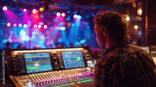 A sound engineer mixes audio levels while a band performs on stage surrounded by colorful lights.