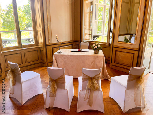 Elegant dekorierter Raum für eine standesamtliche Trauung mit vier weißen Stühlen und goldenen Schleifen, festlich gedecktem Tisch, Kerzen und Blumen, in historischem Ambiente mit Holzvertäfelung.