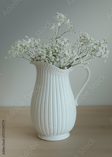 Elegant white ceramic pitcher filled with delicate white baby's breath flowers, creating a minimalist and serene still life composition