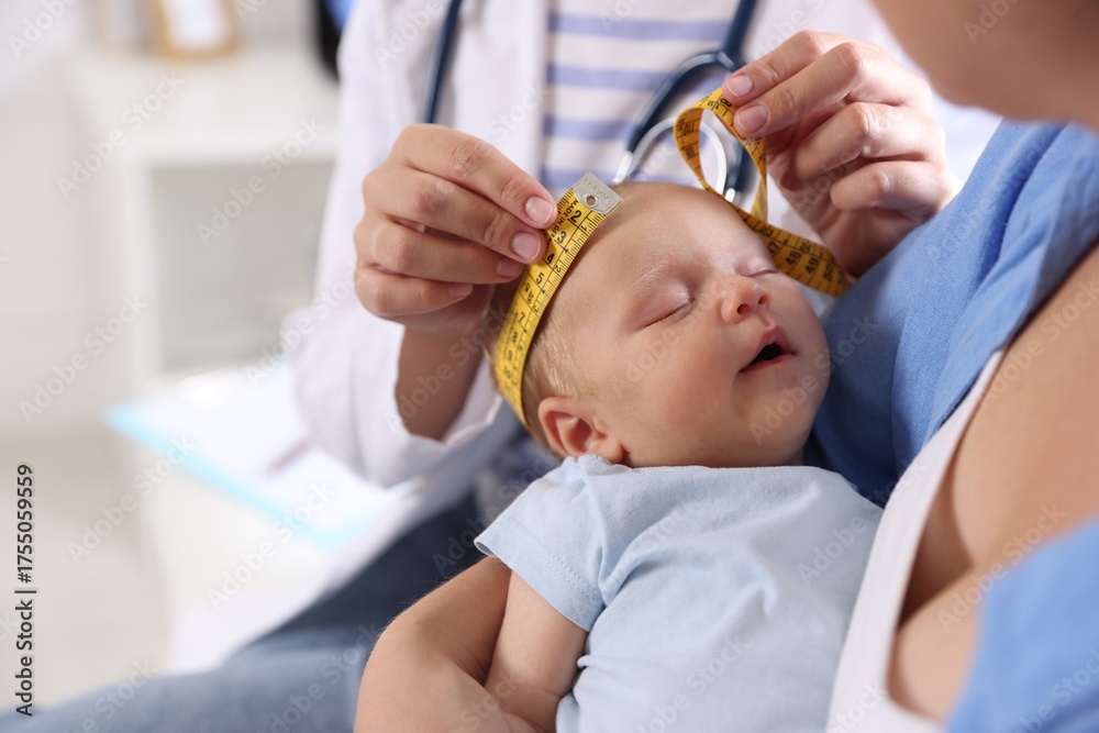 Fototapeta premium Mother and her cute little child having appointment with pediatrician in hospital, closeup. Doctor measuring baby's head