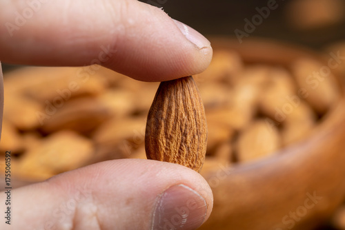 yellow-brown unroasted almonds in a person's hand, a large amount of hard raw almonds is held in the hand against the background of other nuts