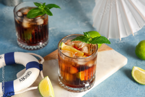 Photography Glasses of cold Cuba Libre cocktail with toy ring buoy and umbrella on blue grun