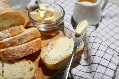 Wooden board with sliced bread, butter and jug of cream on grey grunge background