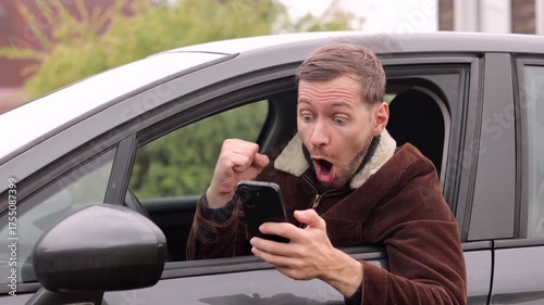Happy satisfied man looking at smartphone screen gesturing yes with clenched fist and screaming inside the car.