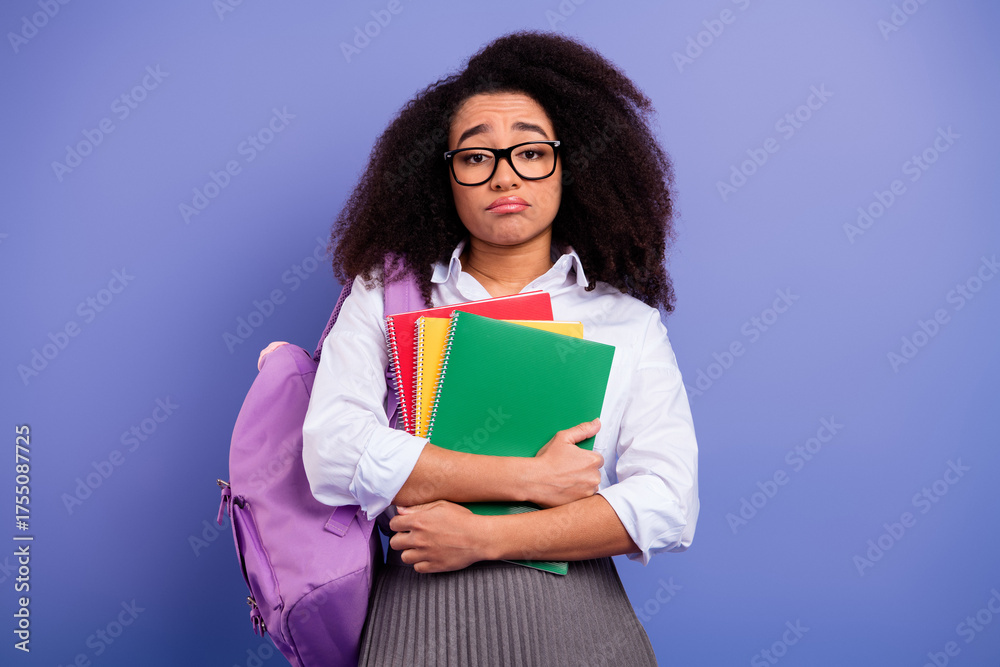 Obraz premium Young student with colorful notebooks and a backpack expressing a thoughtful mood on a purple background