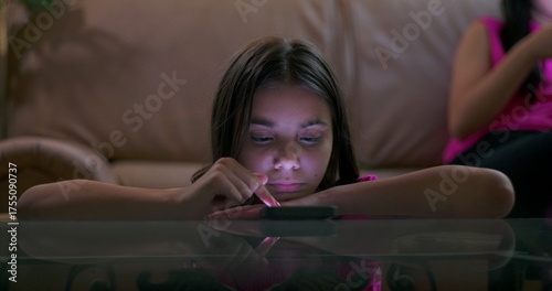 Fotografija Child engrossed in smartphone, lying on table in living room, showing signs of s