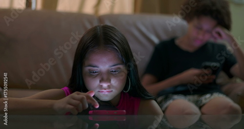Photos Young girl focused on smartphone lying on table with glowing light on face while