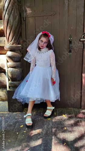 A girl in a white dress and a veil, the image of a scary bride, moves like a zombie on the street, in the park on Halloween