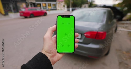 Male hand holding a smartphone with chromakey screen at the city road