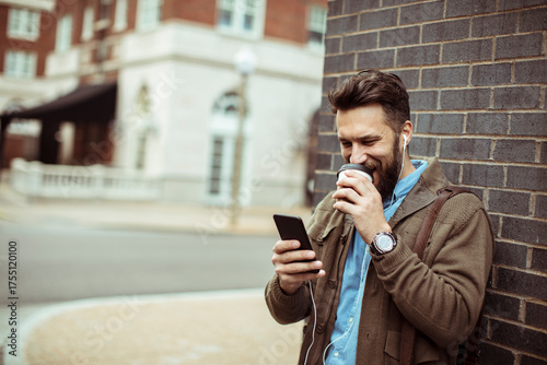 Young adult man drinking coffee and using smartphone outdoors