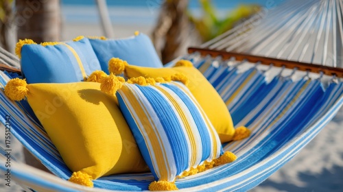 Bright yellow and blue pillows rest on a striped hammock. The scene captures a peaceful beach setting with sunlight reflecting off the waves in the background.