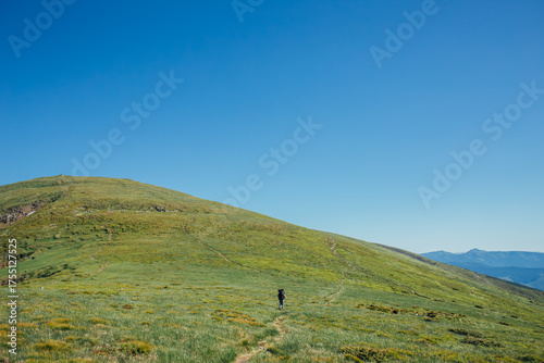 A woman hikes solo with a backpack on a sunny day and mountains on the background