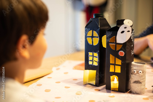 Child boy looking at black halloween haunted houses made with  upcycled packaging. DIY spooky cheap craft idea.
