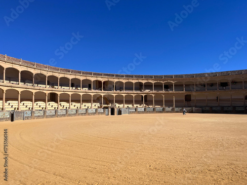 Historische Stierkampfarena in Ronda, Spanien, unter klarem blauem Himmel. Antike Architektur mit Rundbögen und Sandplatz, typisches Beispiel andalusischer Kultur und Geschichte.