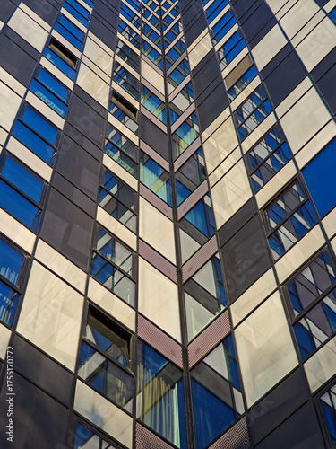 abstract view of a modern skyscraper facade featuring a repeating checkerboard pattern of dark panels and reflective windows in shades of blue and white.