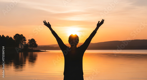 Silhouette of a man with raised arms from behind, looking at the sunset.