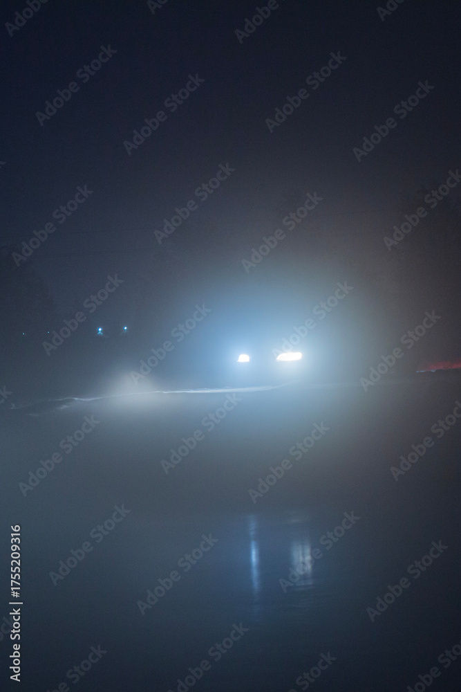 Fototapeta premium a car with fog lights on at night, when driving is impossible and dangerous with poor visibility, against the background of the night sky and slippery roads in winter on ice