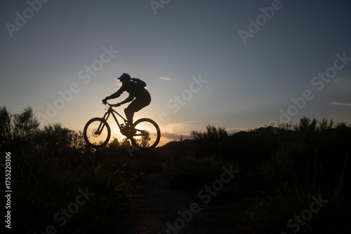 Fotografie Fotografia de silueta de una mujer saltando en una bici de montaña al atardecer,