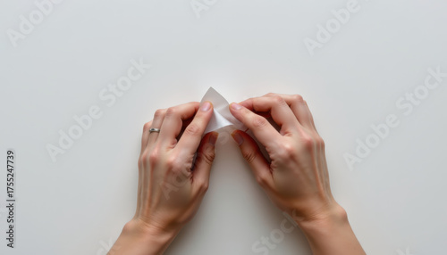 Hands are delicately folding piece of paper, showcasing creative process. soft lighting emphasizes texture of paper and elegance of hands involved in this artistic activity