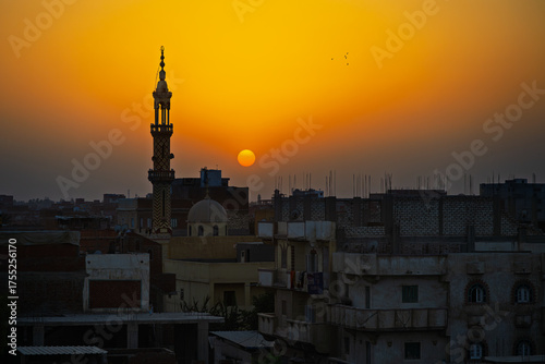 A mosque and minaret silhouetted against a setting sun at golden hour over the city of Cairo, Egypt.