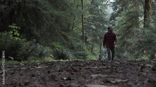 Outdoors hiker walking toward and passing low angle camera on Pacific Northwest trail in old growth forest in half speed, slow motion.