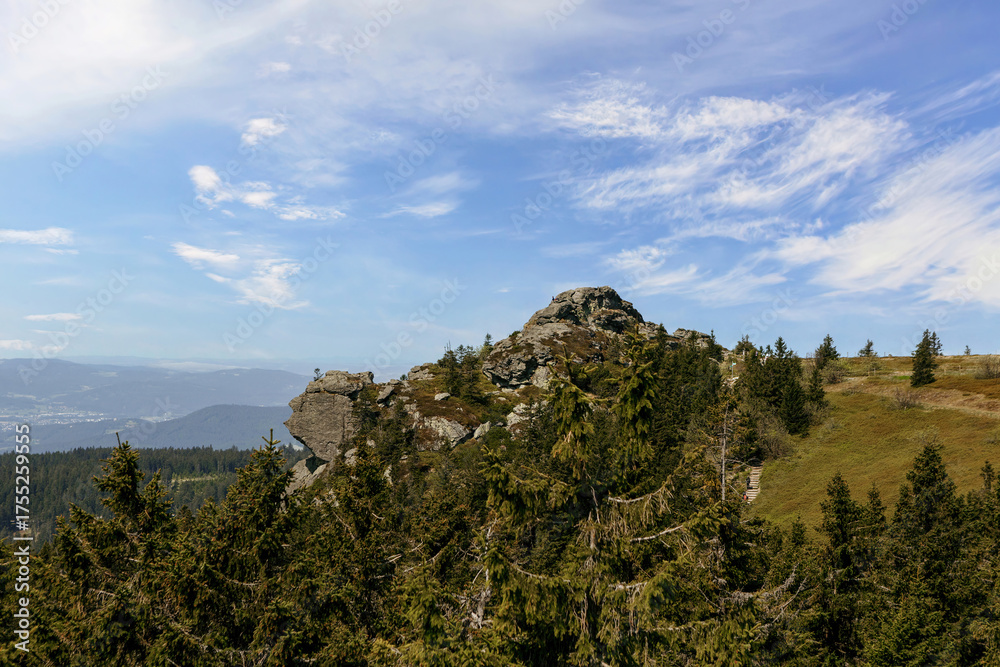Naklejka premium Wide view from the Arber summit in the Bavarian Forest with rocky formations, evergreen trees and a bright blue summer sky.
