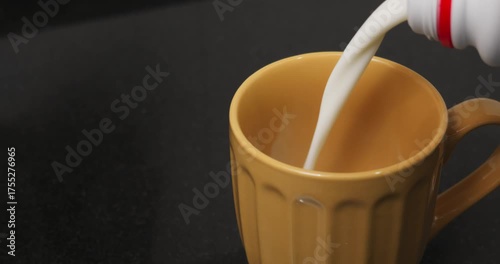 Pouring milk into a large orange glass in slow motion until it is completely full.