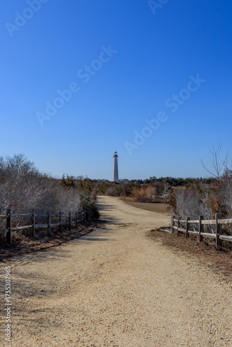 Scenic dirt path leading to a lighthouse under a clear blue sky in a coastal area