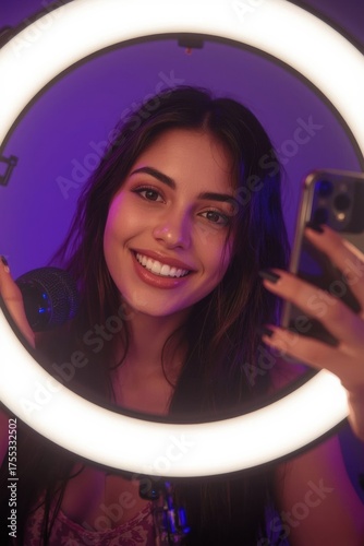 A Young Woman Smiles Brightly While Taking a Selfie Using a Smartphone and Ring Light for Enhanced Illumination