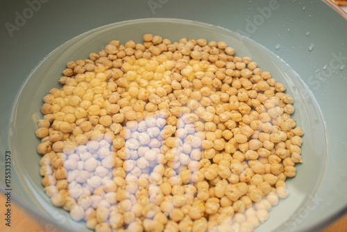 Photograph chickpeas soaking in water in a bowl with natural light next to a window