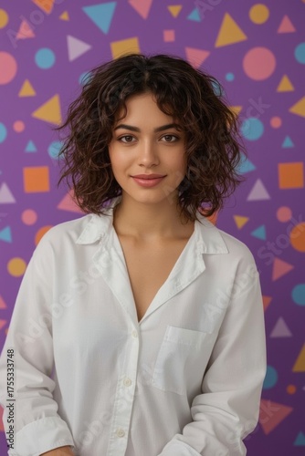 A young woman with curly brown hair and a white shirt posing in front of a colorful geometric background