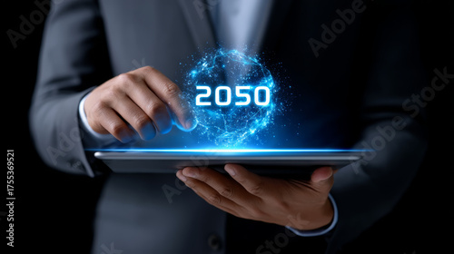 Businessman using tablet with futuristic hologram energy icon, glowing blue sphere, and 2050 text, representing innovation, technology, and digital future vision