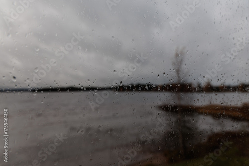 Close-up view of raindrops on a window pane during a rainy autumn day with blurry and moody background, perfect for weather, melancholy, and abstract concepts