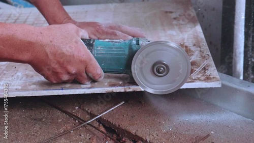 A professional is cutting a ceramic tile with a tile cutter. A professional cutting a tile using an angle grinder at construction site. A professional is cutting tiles.
