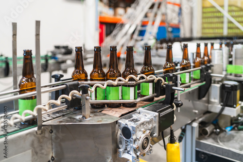 Slika na platnu Beer bottles with green labels traveling on a conveyor belt in a modern brewery,