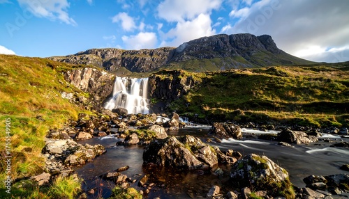 A scenic landscape of a waterfall cascading over rocky terrain with a mountain as the backdrop. The sky is blue and partially cloudy