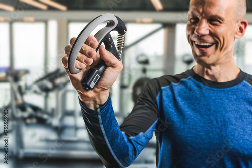 Happy athletic man using grip strengthener to enhance hand and forearm muscles. Smiling man squeezing adjustable hand gripper in modern gym environment