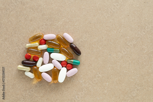 Top view with copy space of assorted supplement pills and capsules on a light brown wooden background. Health insurance, and minimal medical concept.