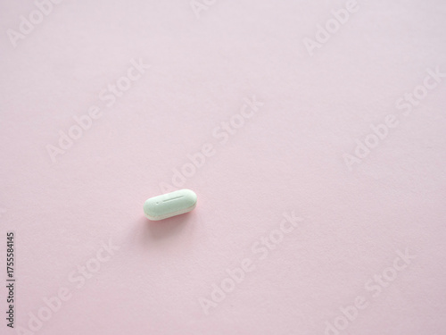 Single white vitamin supplement pill on a pink background. Close-up copy space. Health supplement concept.