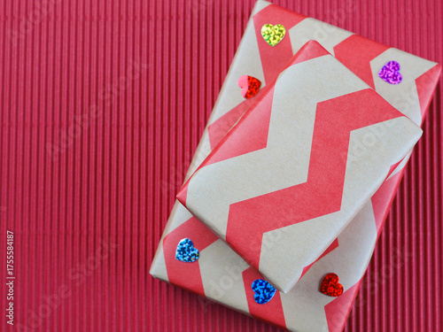 Top view of two gift boxes wrapped in red zigzag kraft paper with small flowers on red corrugated paper background. Concept for happy birthday, thank you, mother's day, anniversary, Valentine's day.