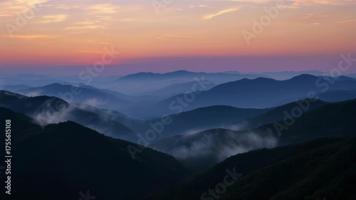 Misty mountain range at sunset with a colorful sky, the sun visible