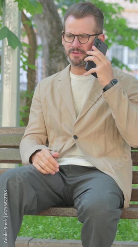 Angry Young Man Talking on Phone in Argument while Sitting Outdoor, Vertical Video