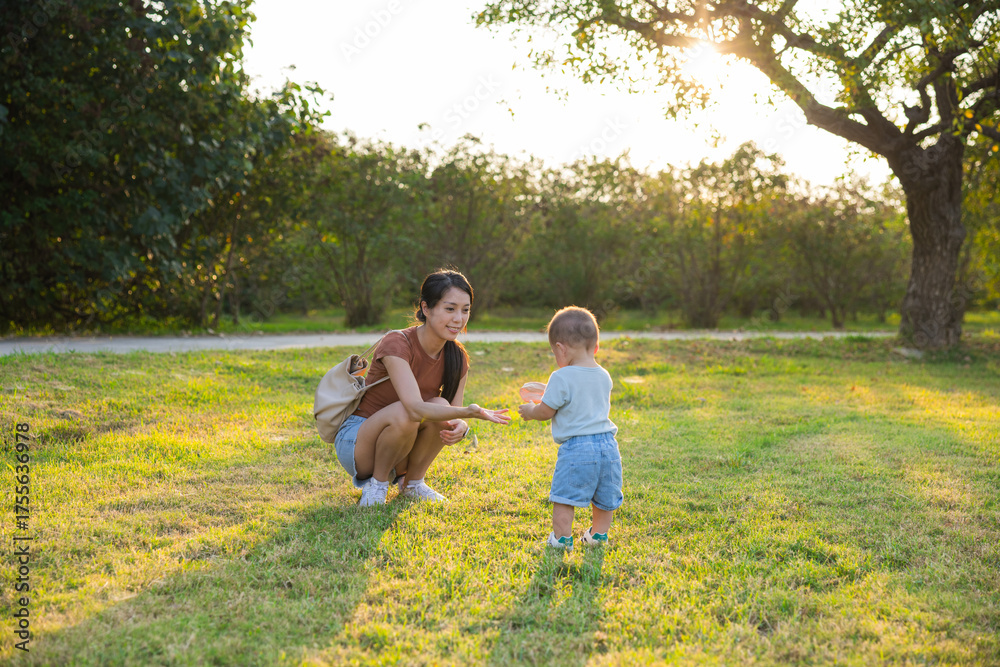 Fototapeta premium Mother holding baby son walking together at sunny park