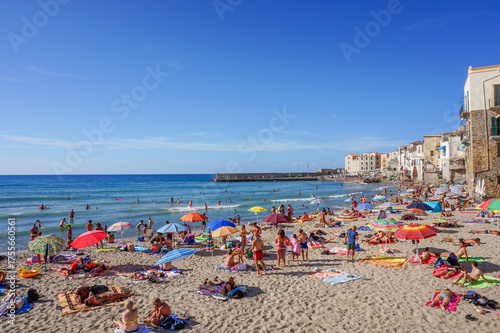 Fotografie A busy summer day on the sandy beach of Cefalù, Sicily, with tourists sunbathing
