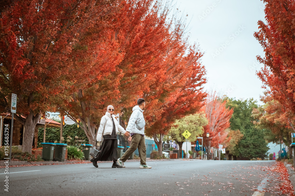 Obraz premium Couple strolling down a tree-lined street with stunning autumn colors.
