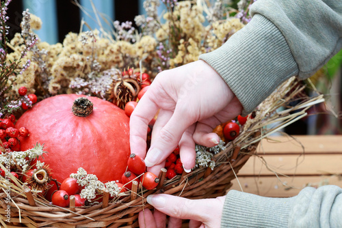 Florist at work: woman shows how to make seasonal autumn table decoration with pumpkins, flowers and plants in a wicker basket.