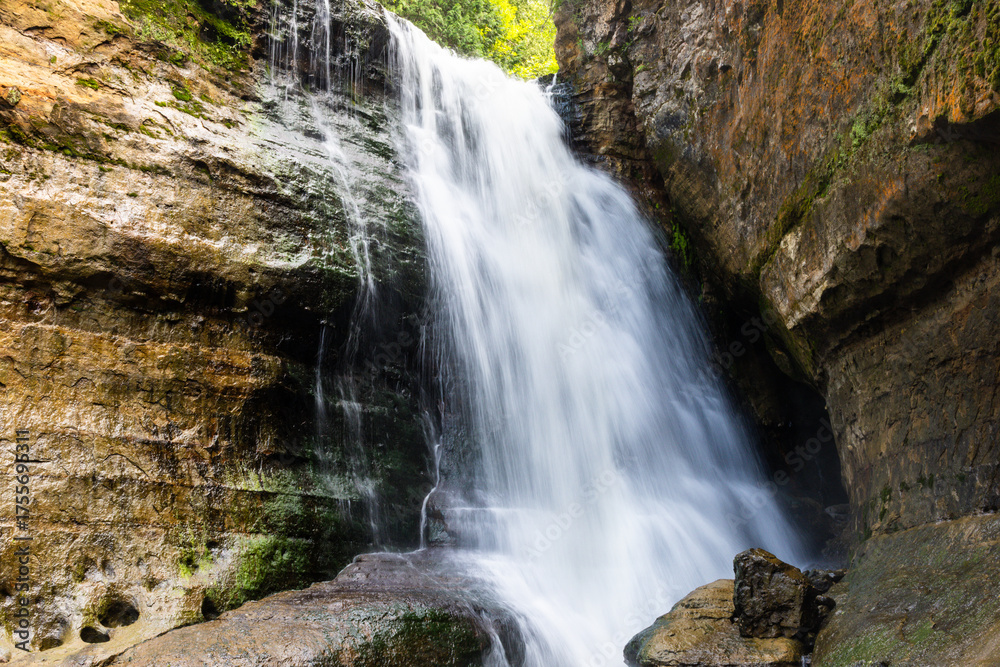 Fototapeta premium Waterfall and cliff surrounded by greenery in summer