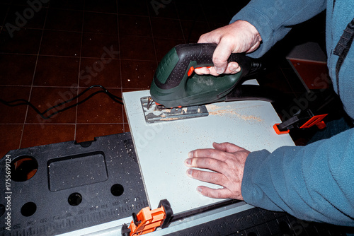 Lateral and semi zenithal image of a man cutting wood with a cutting machine. He is leaning on a workbench. The do-it-yourselfer 