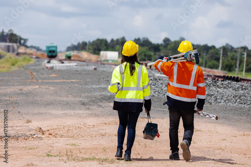 Foto Two engineers wearing safety helmets and reflective jackets walk together at a railway construction site carrying surveying tools