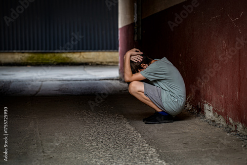 Scared fearful small boy covering face. Boy shouts covered his face with his hands, bullying. A lonely boy sits in tunnel. Sad child suffering from depression sitting alone in alley loneliness